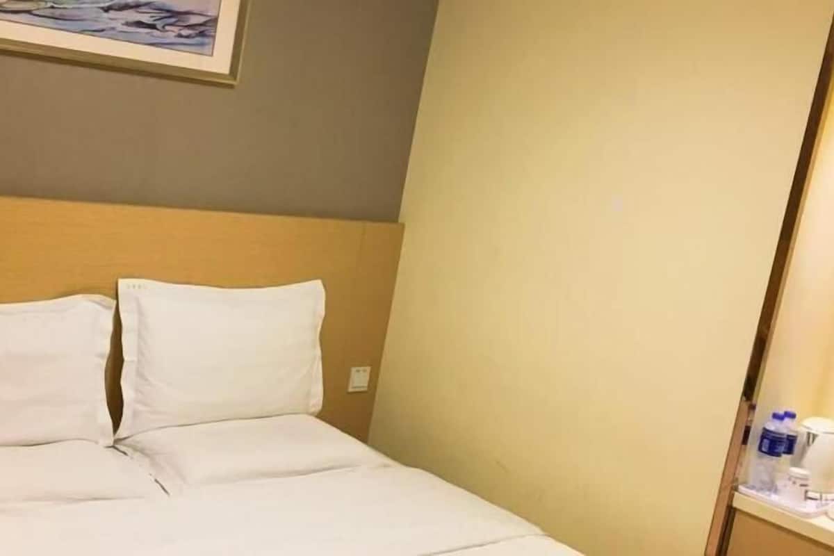 A hotel room with a bed, a headboard, a wall-mounted painting, and a side table with a bottle and a container.