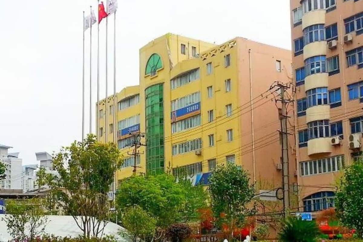 A multi-story building with a green circular sign, multiple windows, and several flags on flagpoles.