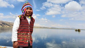 Una persona de pie junto a un lago tranquilo, con montañas al fondo.