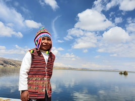 Una persona de pie junto a un lago tranquilo, con montañas al fondo.