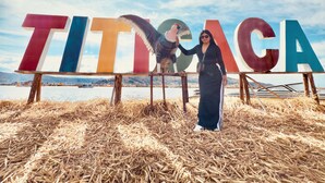 Una persona de pie frente a letras grandes y coloridas que deletrean 'TITICACA', con un paisaje montañoso de fondo.