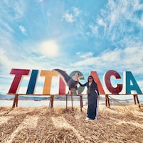 Una persona de pie frente a letras grandes y coloridas que deletrean 'TITICACA', con un paisaje montañoso de fondo.
