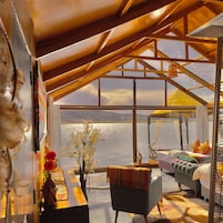 Una habitación con un ventanal grande, una cama, una silla, una mesa y una mesita de noche con un jarrón de flores.