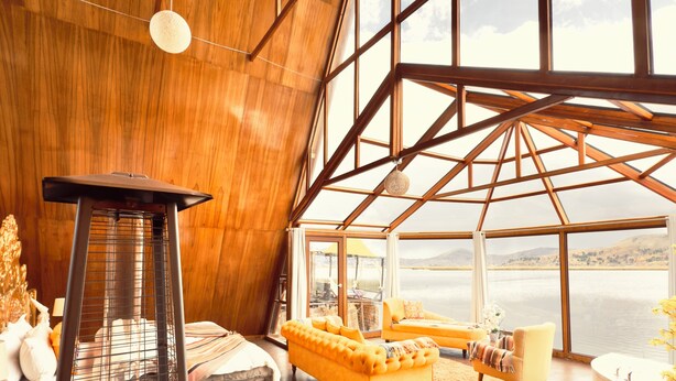 Una habitación amplia con techo alto, un ventanal grande, un sofá, una silla y un radiador.