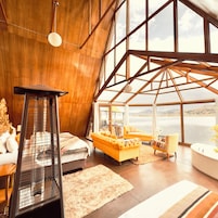 Una habitación amplia con techo alto, un ventanal grande, un sofá, una silla y un radiador.