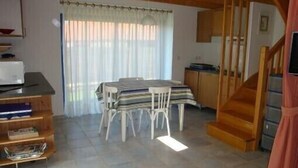 Une pièce chaleureuse comprenant une table à manger, des chaises, un escalier en bois et un coin cuisine.