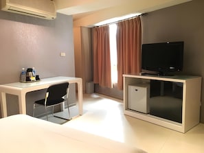A hotel room with a desk, chair, television, and a small refrigerator. - Daylight Hotel (New Taipei City)