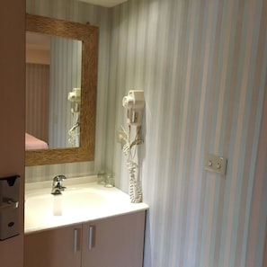 A bathroom with a striped wallpaper, a white sink, a mirror with a wooden frame, and a hairdryer mounted on the wall. - Daylight Hotel (New Taipei City)