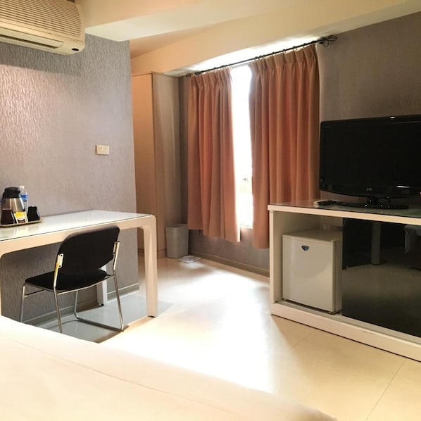 A compact room with a desk, chair, television, and a small refrigerator. - Daylight Hotel (New Taipei City)