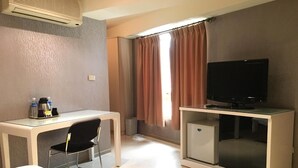 Quarto de hotel com cama, escrivaninha, cadeira, televisão e mini-geladeira.