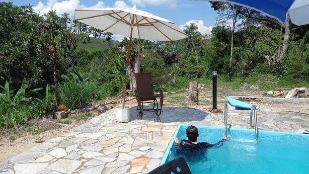 A swimming pool with stone tiles, a chair, and an umbrella. - SITE REFUGIO DO RIO - BANANAL - SP (BANANAL)