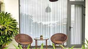 A patio area with wicker chairs and a small table, surrounded by green plants. - Hoi An Cabbage Garden (Da Nang)