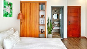 A bedroom with a bed, a wooden wardrobe, a potted plant, a bathroom with a mirror, and a red door. - Hoi An Cabbage Garden (Da Nang)