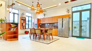 A modern kitchen with wooden cabinets, a dining area with a table and chairs, and a large window providing natural light. - Hoi An Cabbage Garden (Da Nang)