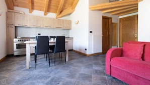 Cocina compacta con armarios de madera, una mesa de comedor con sillas, un sofá rojo y techo de madera.