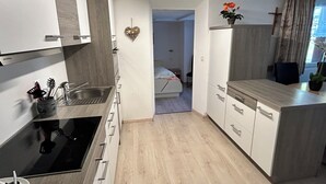 Una cocina moderna con estufa integrada, un lavamanos y una encimera. Se ve una cama al fondo.