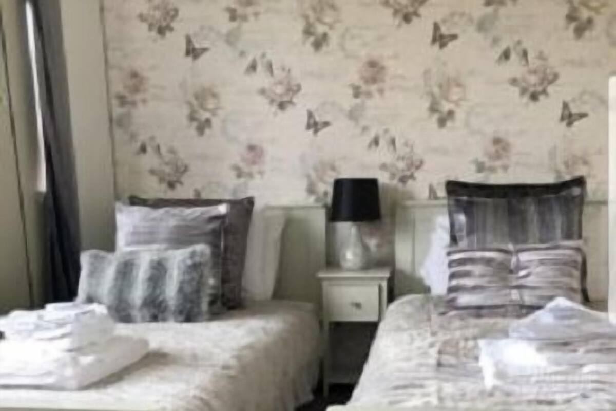 Un dormitorio con dos camas, una mesita de noche, una lámpara y papel tapiz con motivos florales.