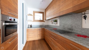 Une cuisine moderne avec des meubles en bois, un four Bosch, des plans de travail en granit et une fenêtre au-dessus de l’évier.