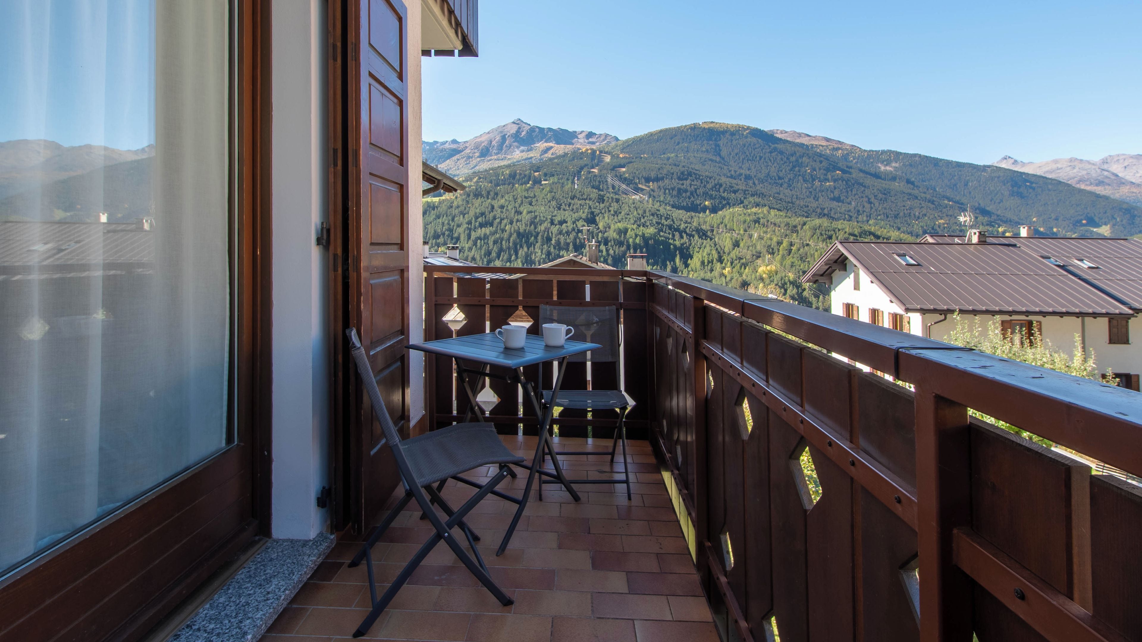 Un balcon avec une table et des chaises, donnant sur un paysage montagneux.