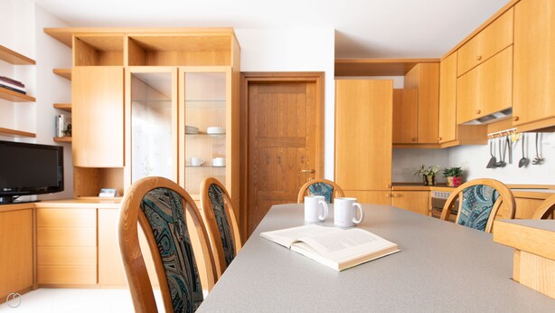 Una cocina moderna con armarios de madera, una mesa de comedor con sillas, un televisor y una estantería.