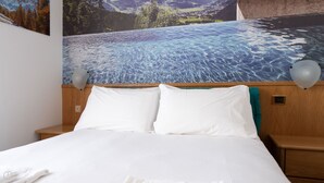 Habitación de hotel con cama, cabecero de madera, almohadas blancas y un cuadro de un paisaje montañoso.