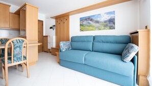 Una sala de estar moderna con un sofá azul, muebles de madera y un cuadro de un paisaje montañoso en la pared.