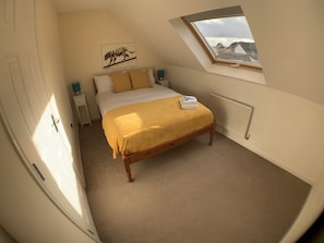 Une chambre à coucher comprenant un lit, une table de chevet, une commode, un radiateur et une lucarne.