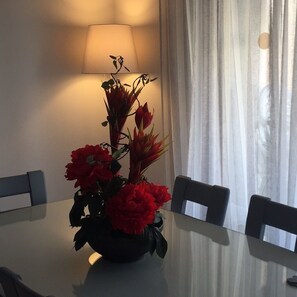 A dining table with a floral centerpiece, a lamp, and chairs in a room with a window and curtains. - ATTILA apartment by the sea (QUARTEIRA)