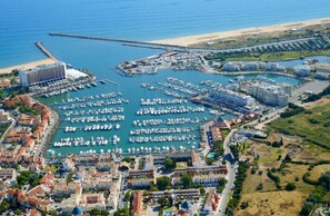 An aerial view of a coastal marina with multiple docks, a large hotel, and residential buildings.