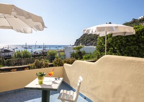 Una terraza con una mesa, dos sombrillas blancas, una planta en maceta y una bebida.