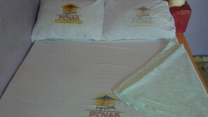 A bed with two pillows and a blanket, each featuring a logo with the text "PENAS". - Club Panas (Bondo)