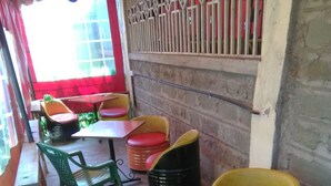 A café with wooden tables and colorful chairs, a brick wall, and a window with a metal railing. - Club Panas (Bondo)