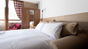 A hotel room with a bed, a sofa, a chair, a wardrobe, and a lamp. - Plagheira 1 - Studio Apartment, Sleeps 2 (Valfurva)