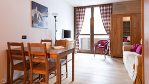 A dining area with a wooden table and chairs, a television, and a painting on the wall. - Plagheira 1 - Studio Apartment, Sleeps 2 (Valfurva)