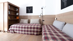 A bedroom with a wooden headboard, a bed with plaid bedding, a nightstand, a bedside lamp, and a bookshelf.