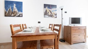 A dining area with a wooden table set for four, two chairs on each side, and a television on a wooden cabinet. - Plagheira 1 - Studio Apartment, Sleeps 2 (Valfurva)