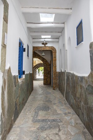 Un estrecho pasillo empedrado de piedra, con paredes blancas y contraventanas azules, que conduce a un arco.
