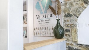 Letrero de 'Vassilia On The Beach' con logotipo de caracola, un expositor de llaves y un jarrón con plantas secas.