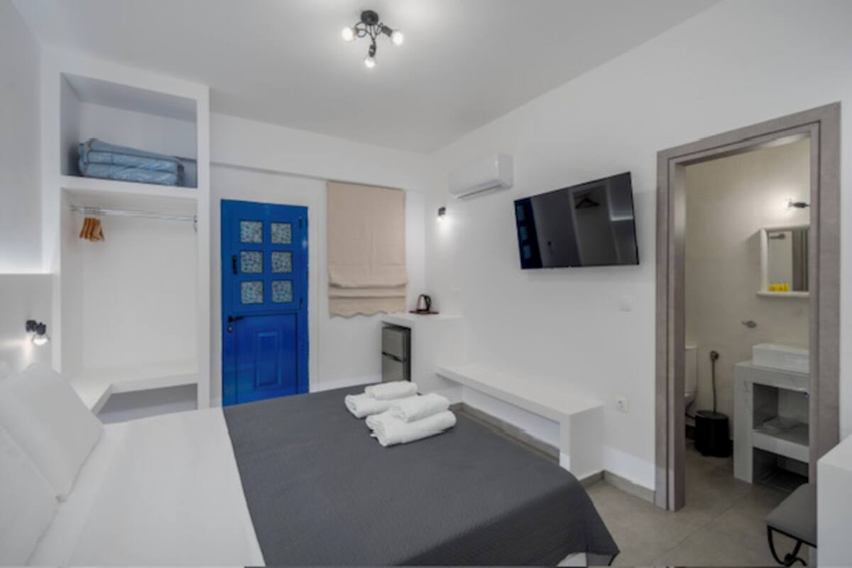 A hotel room with a bed, a blue door, a TV, and a bathroom visible through an open door.