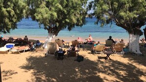 Una playa con tumbonas y gente relajándose bajo los árboles.