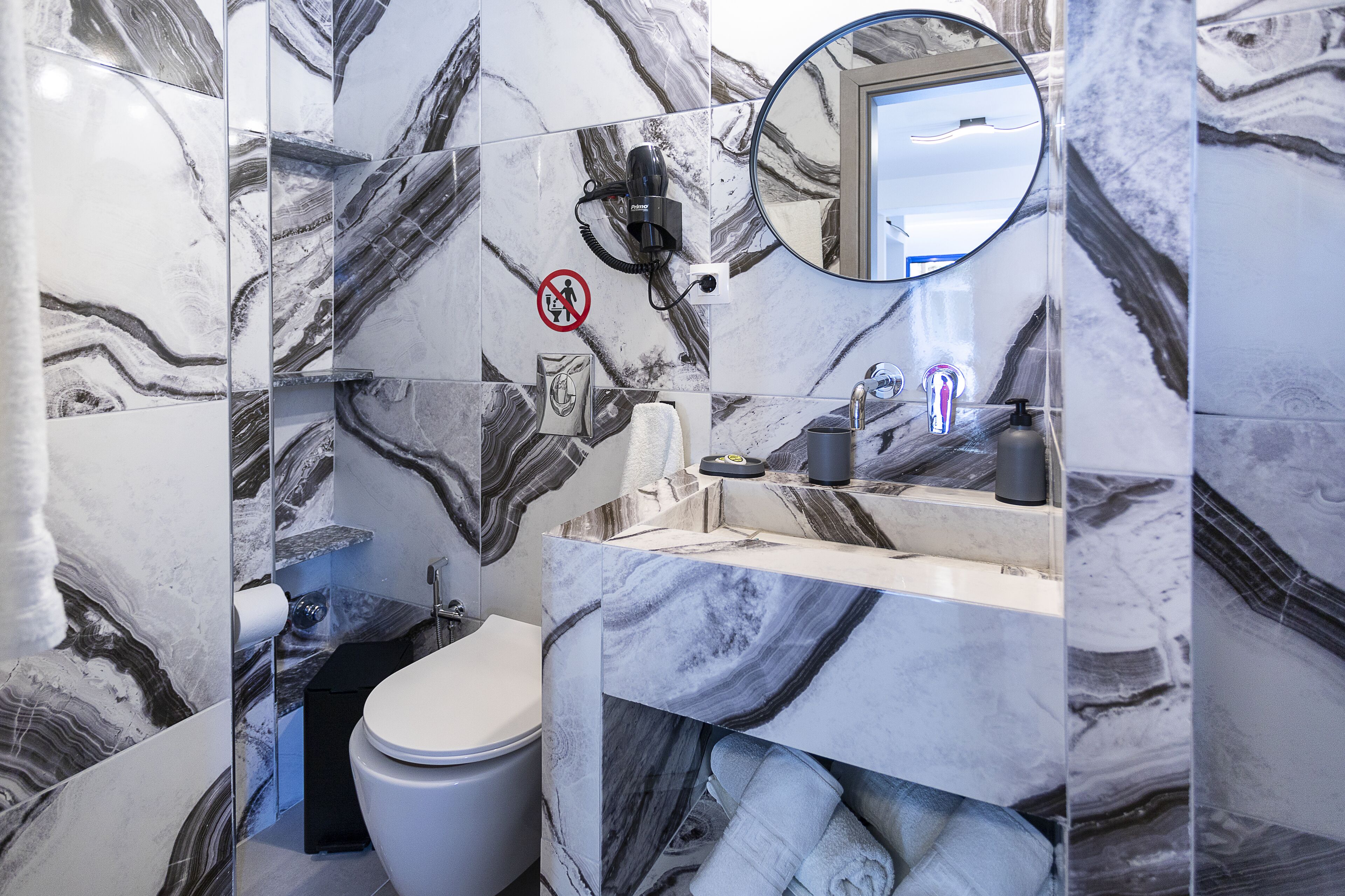 A bathroom with marble walls, a toilet, a sink with a mirror, and a no-smoking sign.
