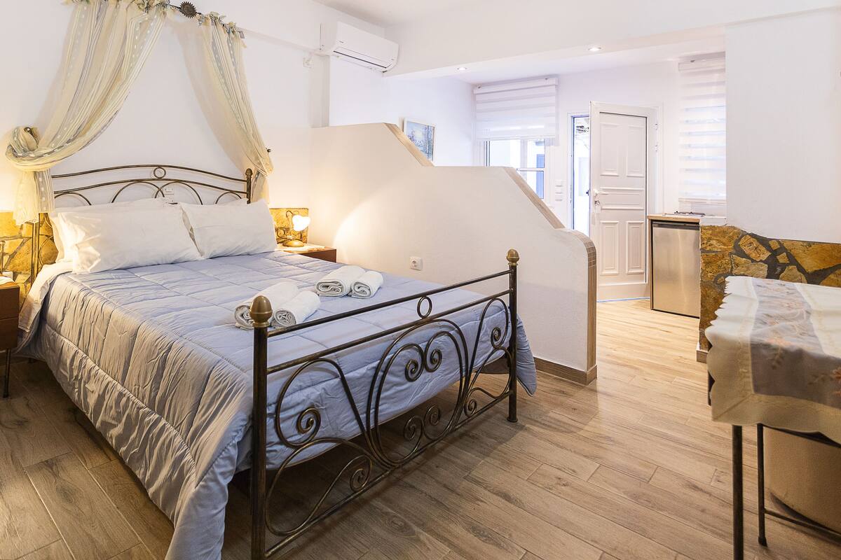 A bedroom with a four-poster bed, a nightstand with a lamp, and a wooden floor.