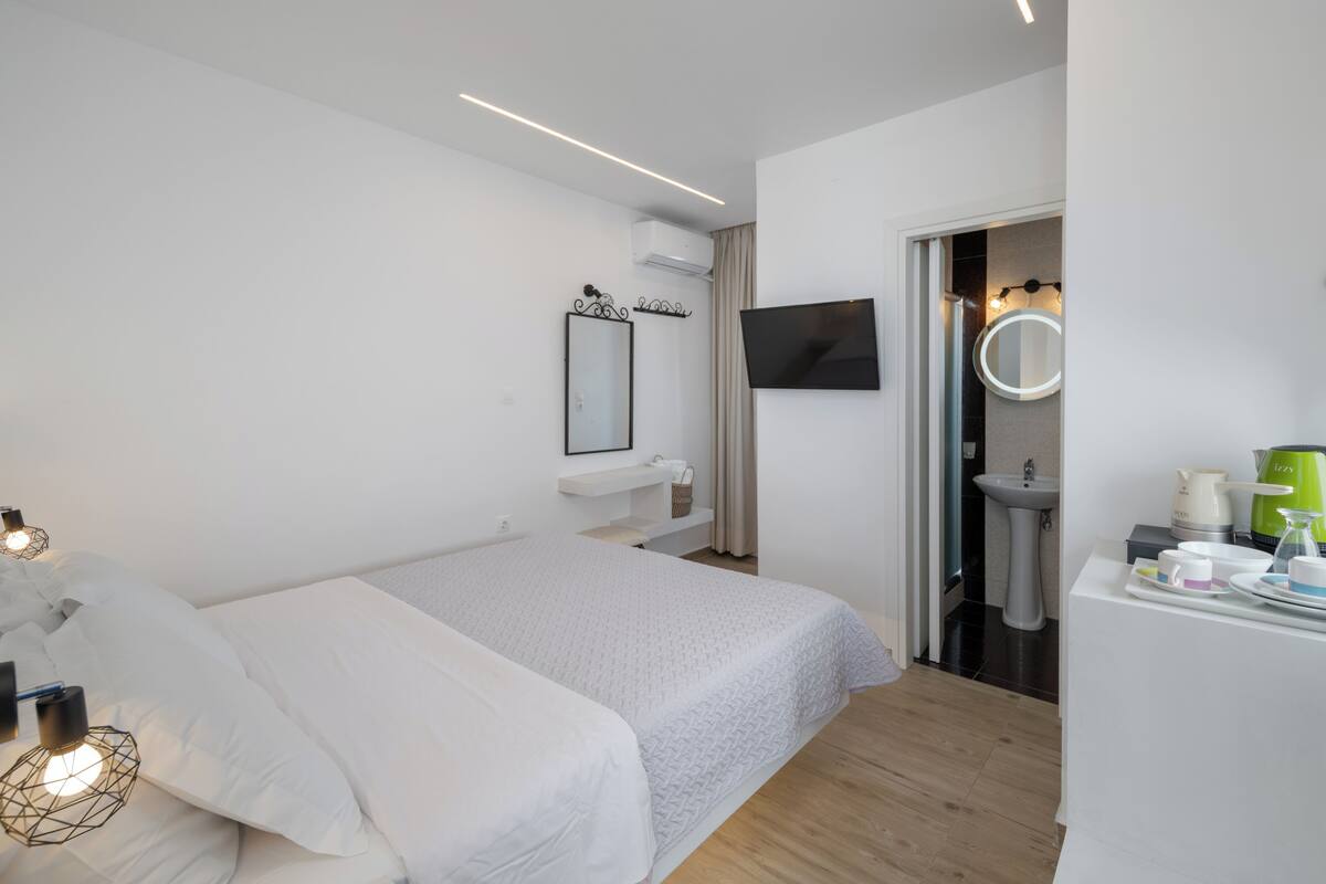 A modern hotel room with a bed, bedside table, TV, and a bathroom with a sink and mirror.