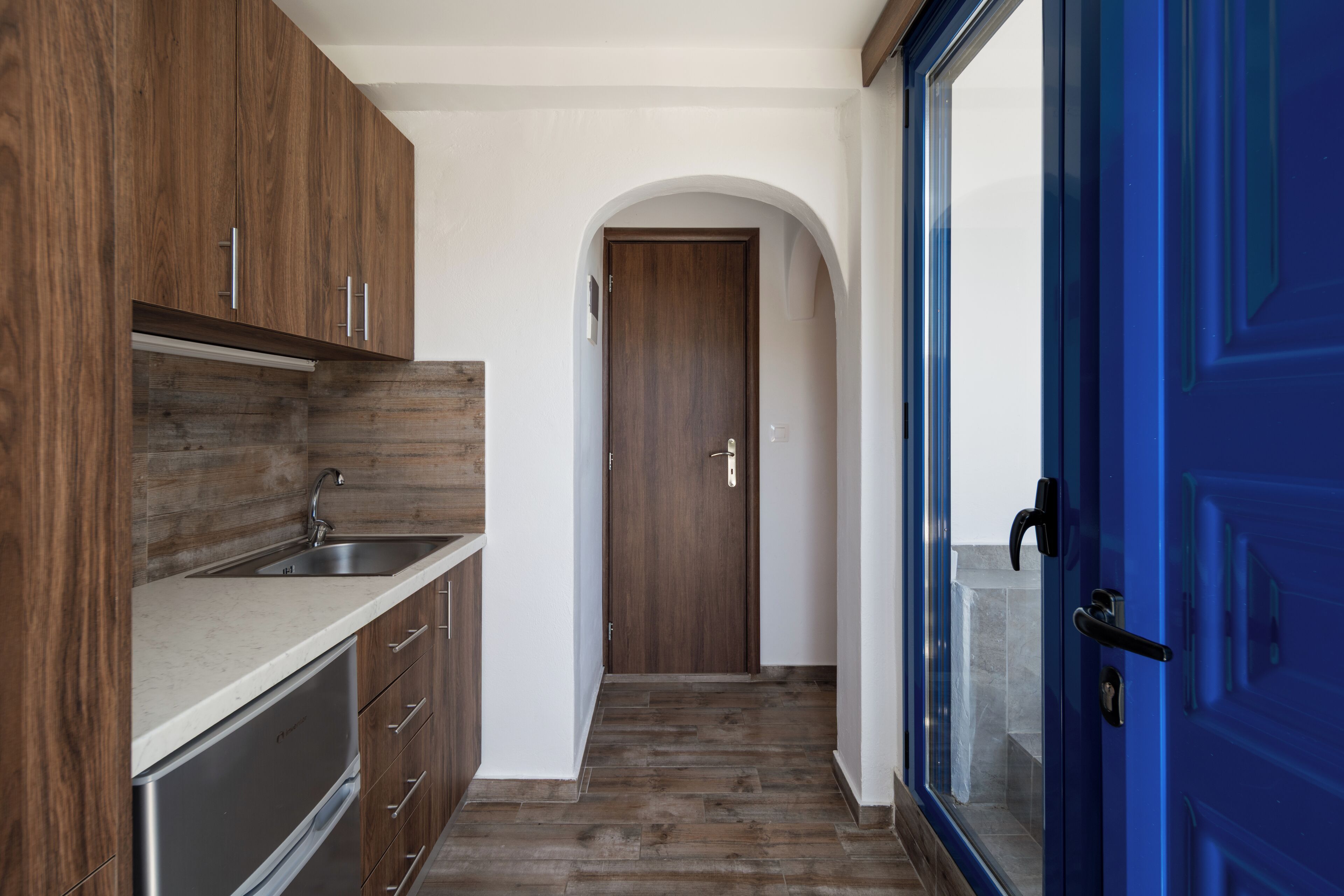 A modern kitchen with wooden cabinets, a stainless steel sink, and a blue door.