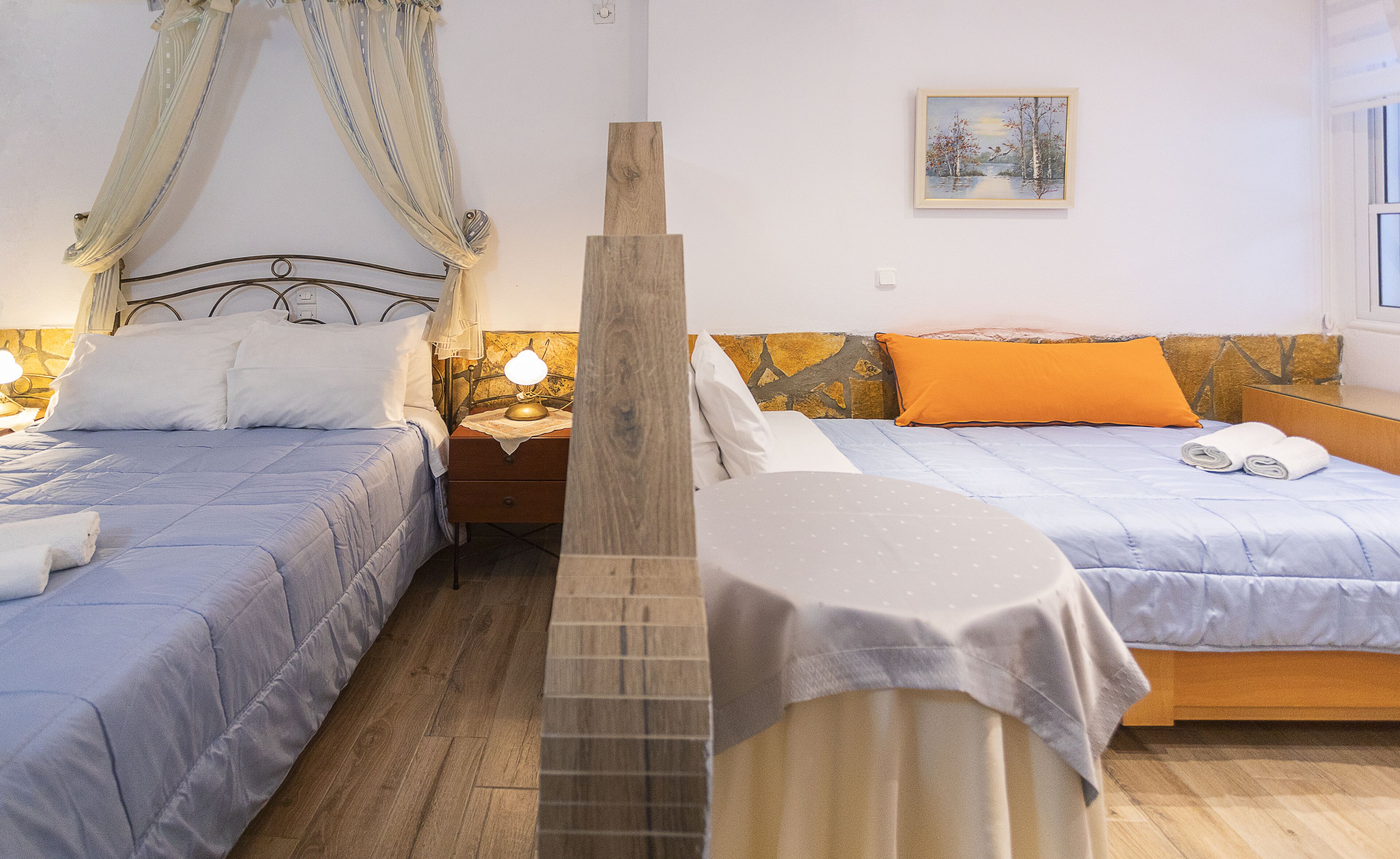 A bedroom with two beds, a nightstand with a lamp, a wooden headboard, and a painting on the wall.