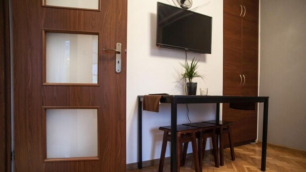 A room with a wooden door, a television mounted on the wall, a small table with two chairs, and a potted plant. - Apartamenty Varsovie Zelazna (Warsaw)