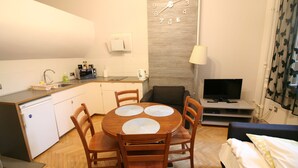A compact living space with a kitchenette, a dining area with a wooden table and chairs, a TV, and a bed with a pillow. - Apartamenty Varsovie Zelazna (Warsaw)