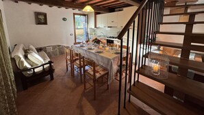 Un comedor con una mesa dispuesta para cuatro, sillas de madera, una araña y una escalera con barandilla.