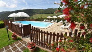 Zona de piscina con valla de madera, sillas de descanso y sombrillas.