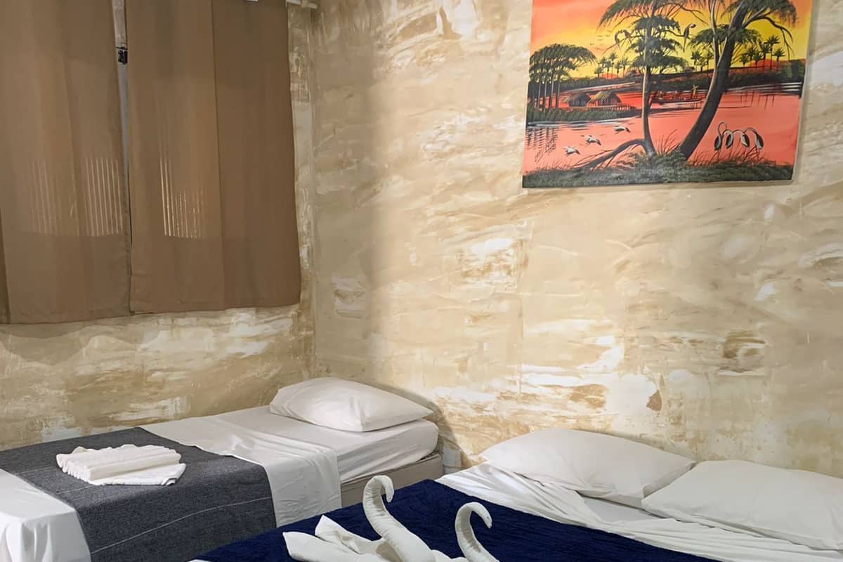 Habitación de hotel con dos camas, cada una con ropa blanca y una manta azul. En la pared, un cuadro que representa una escena de atardecer.